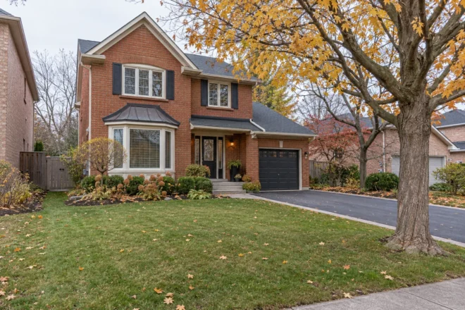 Clear autumn driveway beside an open lawn and mature maple at a red-brick house.