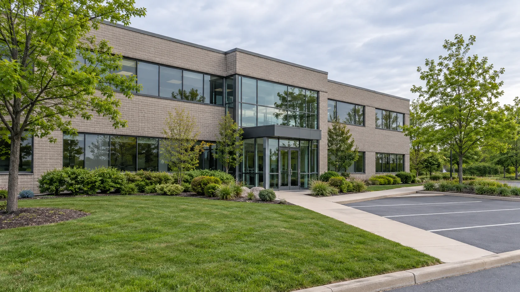 Low-rise office building with front lawn, low planting and a clear concrete entry walk beside parking.