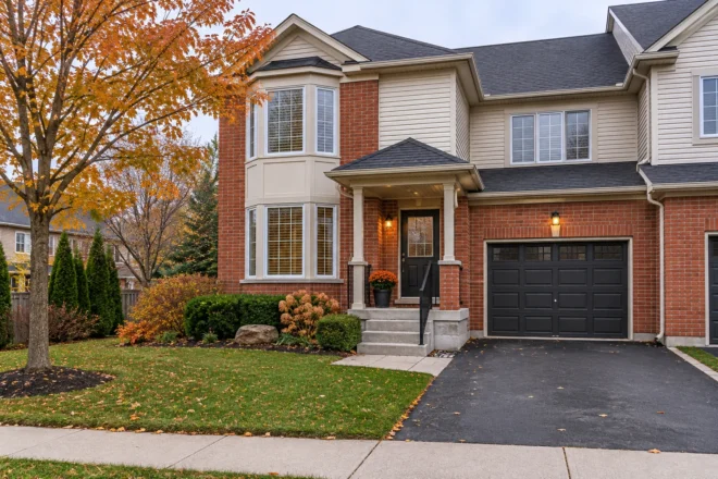 Tidy townhouse front steps and driveway beside a small autumn lawn and shrub bed.